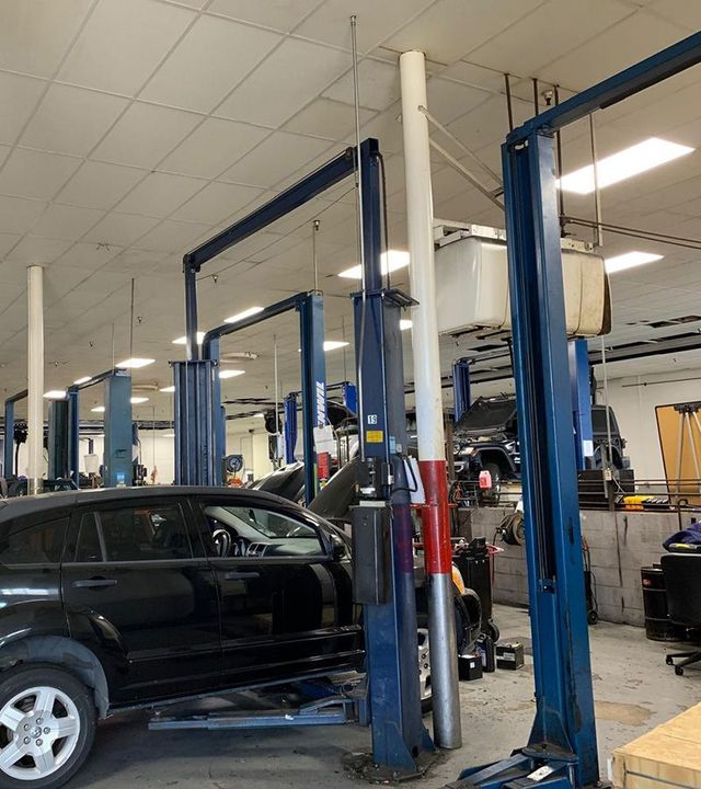 Black SUV in an auto repair shop with blue vehicle lifts and a mechanic working nearby