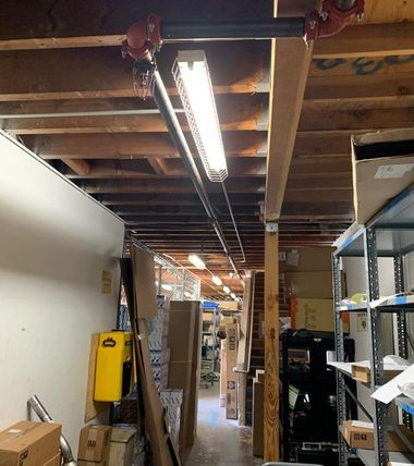 Narrow industrial storage hallway with exposed ceiling, fluorescent light, shelves, and boxes.
