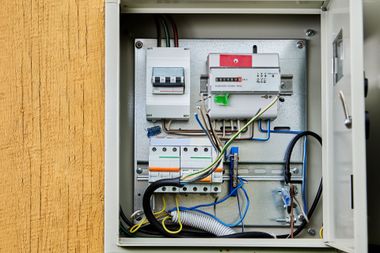 Open electrical panel with circuit breakers, wires, and utility equipment mounted on a wall.