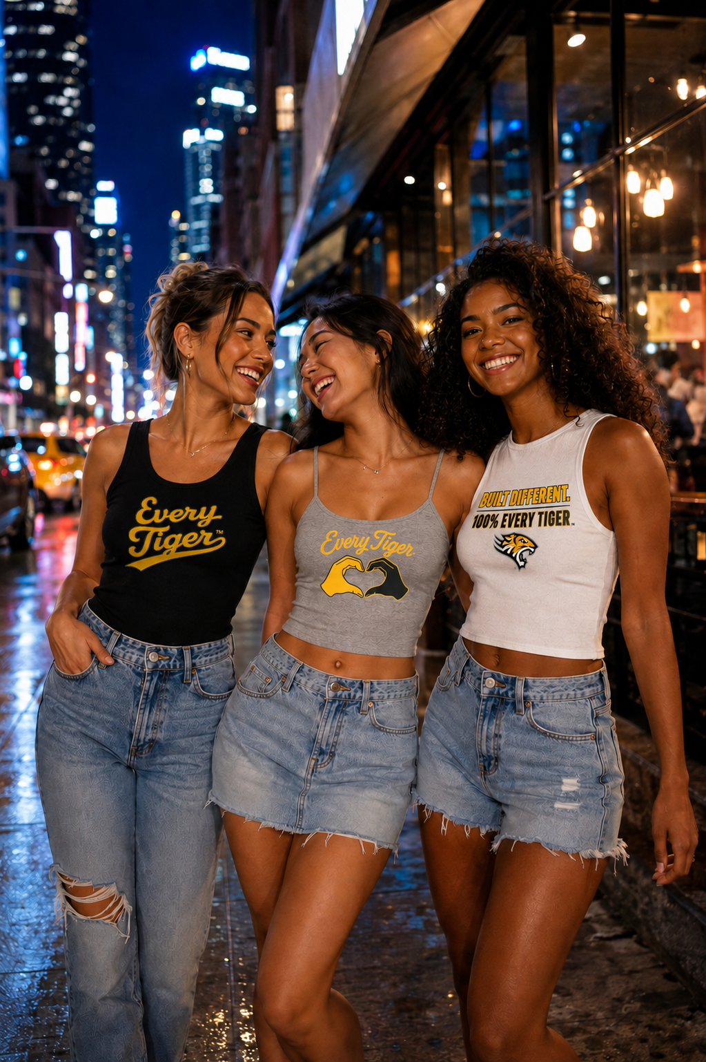 Three friends in cropped tops and denim skirts smile on a city street at night