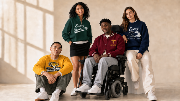 Four people posing indoors, one seated in a wheelchair, wearing colorful sweatshirts against a bright wall.