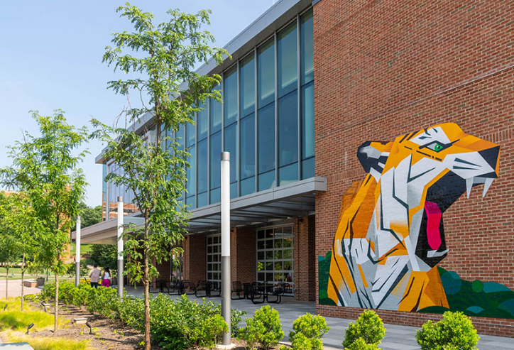 Modern brick building with glass facade and colorful tiger mural on the side