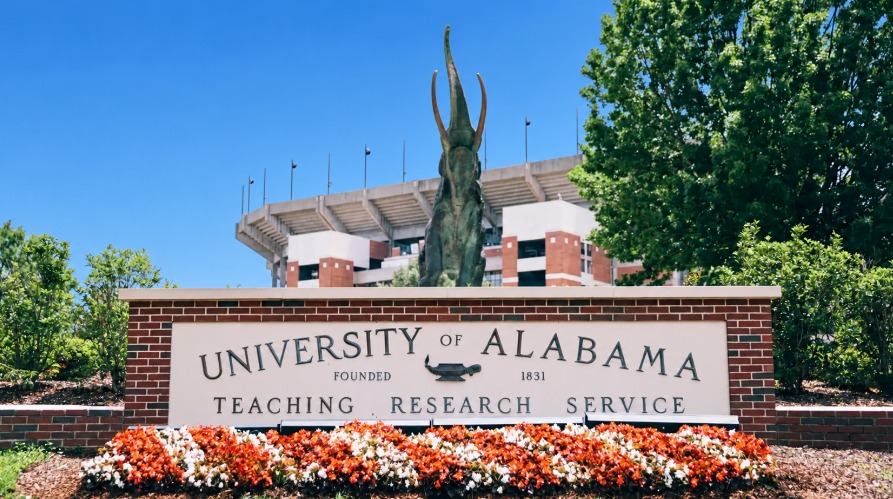 University of Alabama entrance sign with flowers and campus building in the background