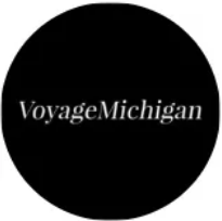 Black circular logo with the white text “VoyageMichigan”
