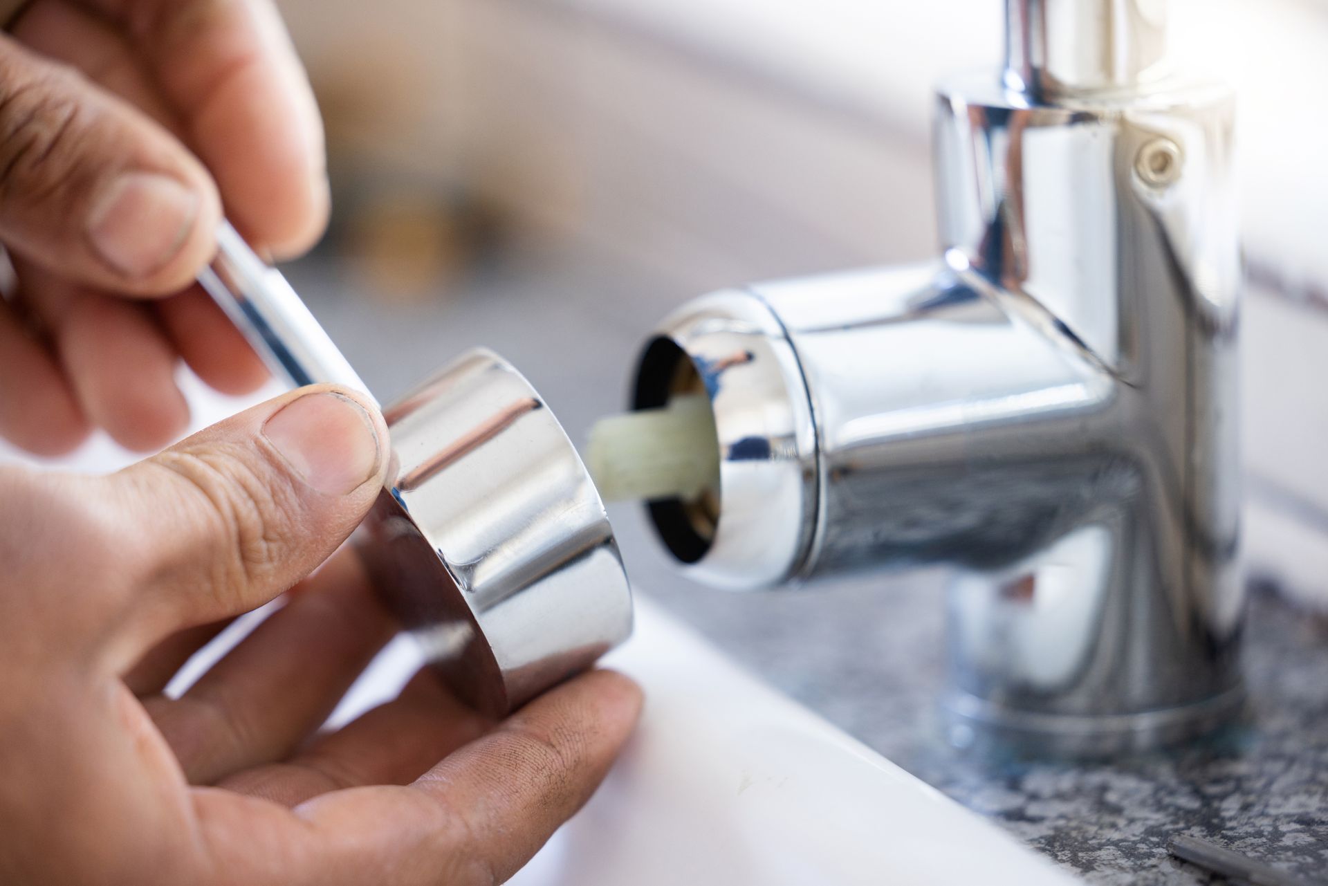 Hands removing a chrome faucet aerator in a sink, with water dripping nearby