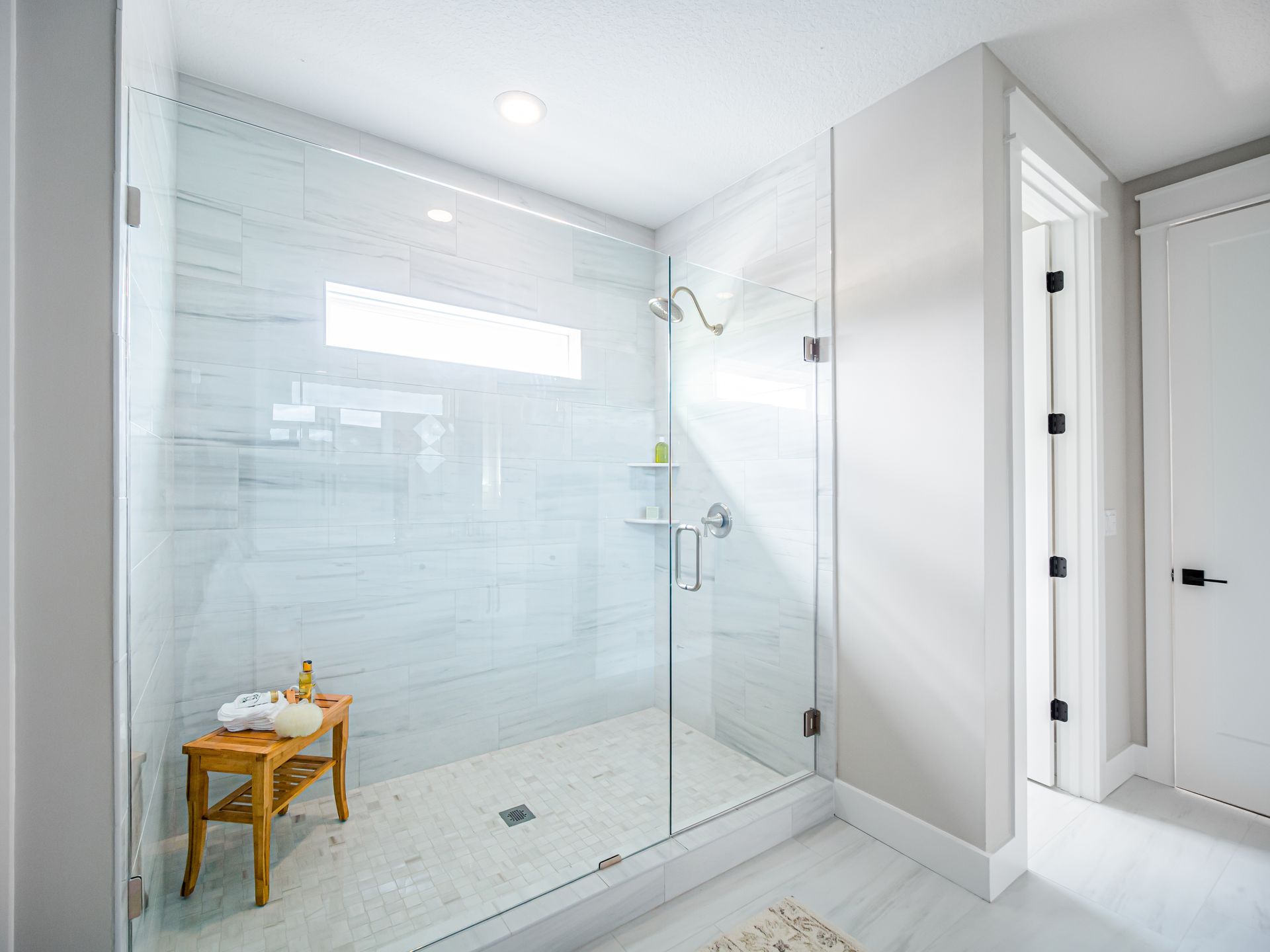 Bright white bathroom with glass shower enclosure and a small wooden stool.