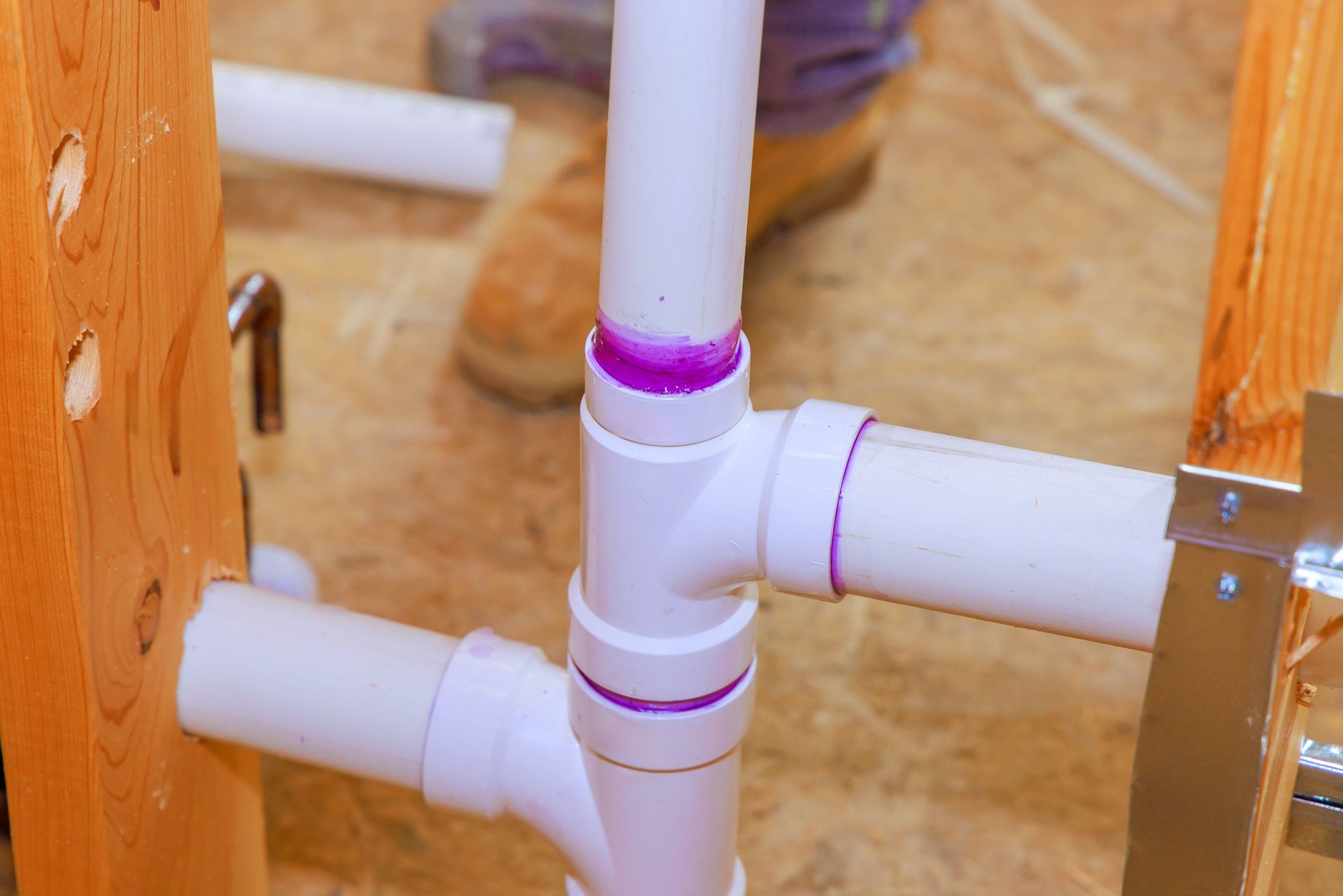 White PVC pipes connected between wooden supports with purple tape, showing plumbing under construction