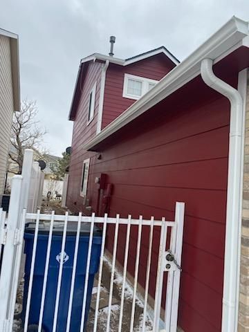 A red house with a white fence and a blue trash can in front of it.