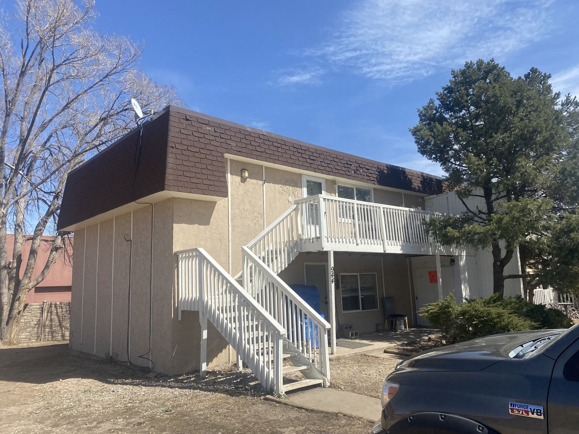 A house with stairs leading up to the second floor and a truck parked in front of it.