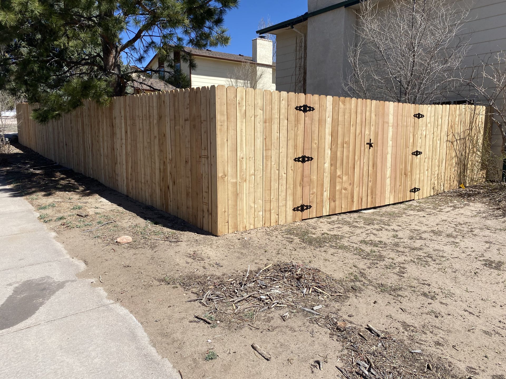 A wooden fence is sitting on the side of a dirt road next to a house.
