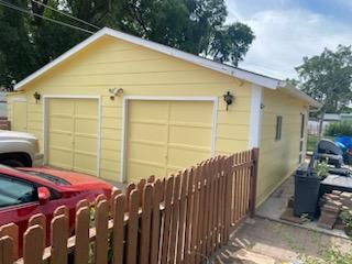A yellow garage with a red car parked in front of it.