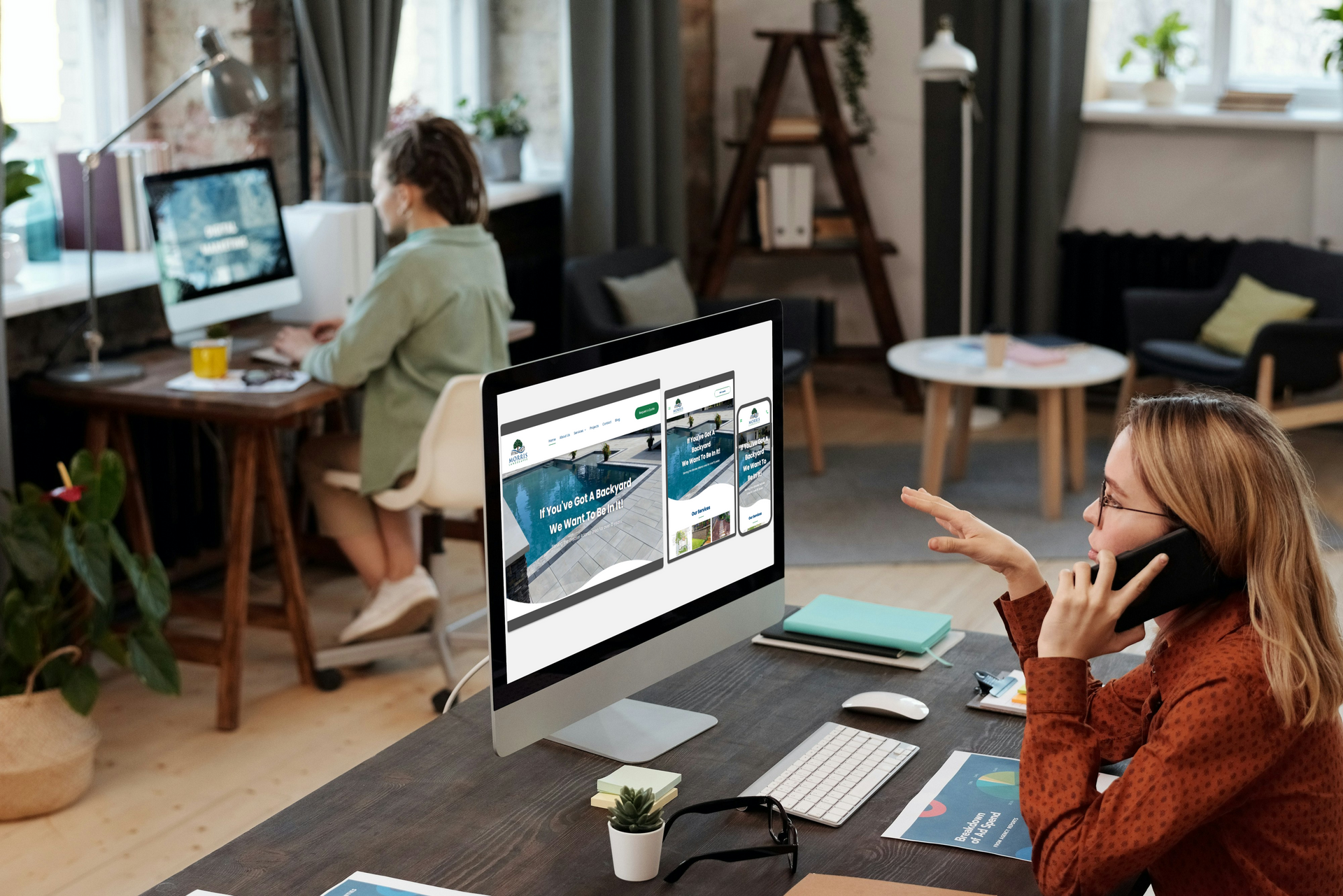 A woman is sitting at a desk in front of a computer talking on a cell phone.