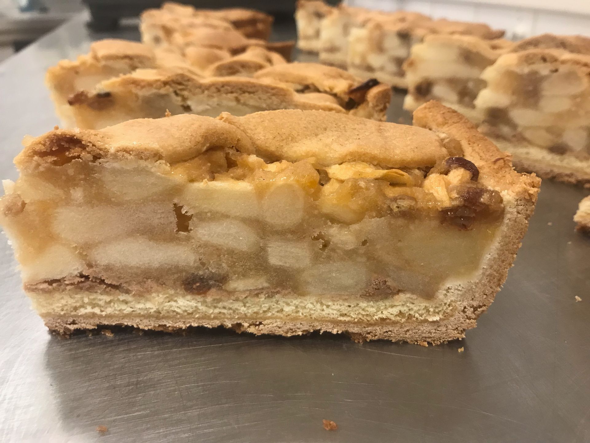 Een plak appeltaart, met een dwarsdoorsnede van appels, deegbodem en topping op een metalen ondergrond.