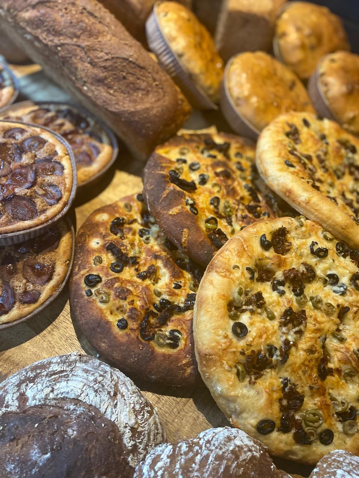 Een assortiment versgebakken brood, waaronder focaccia met olijven en taartjes. Close-up met warme tinten.