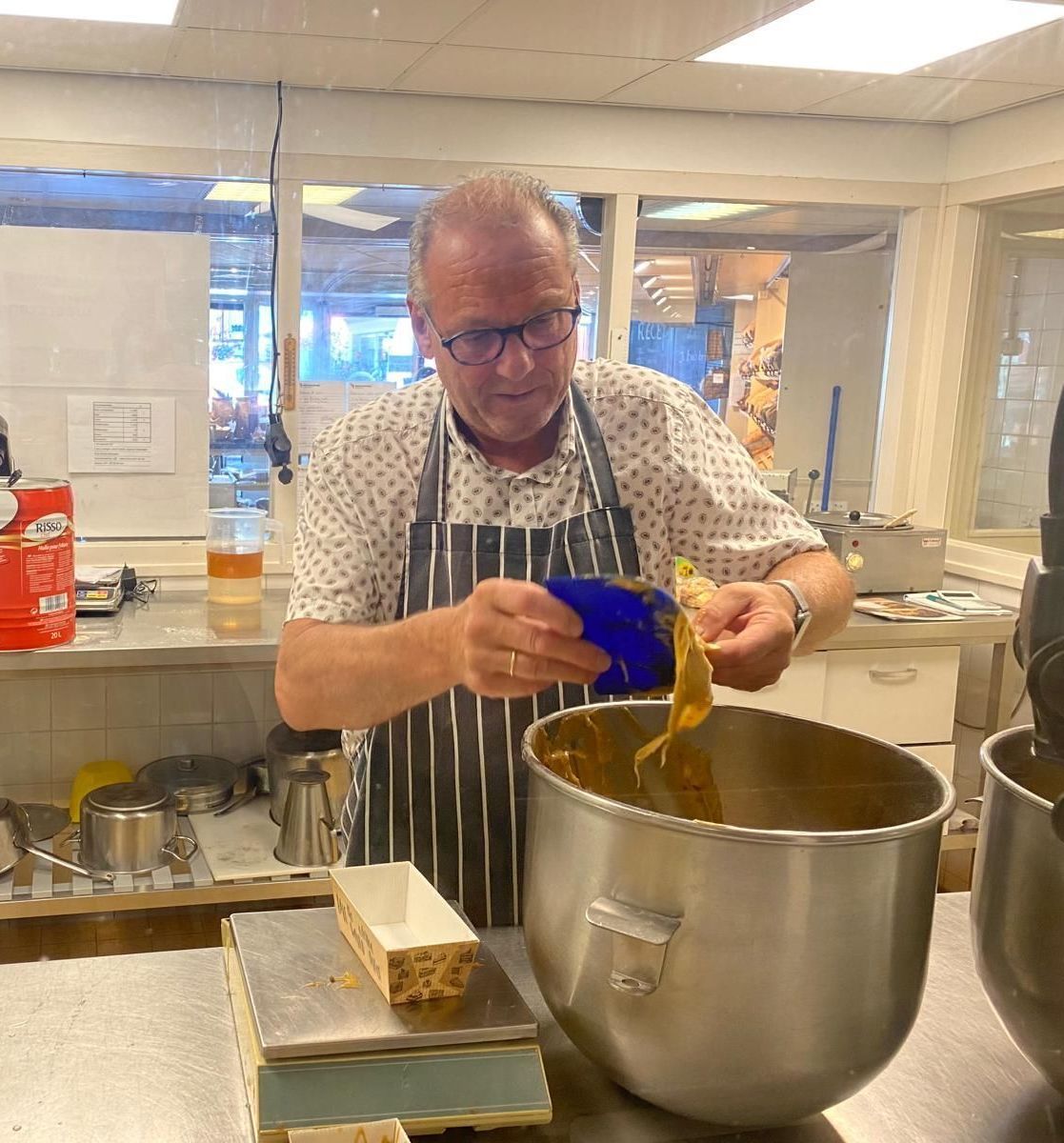 Een man met een schort voegt ingrediënten toe aan een grote mengkom in een keuken.
