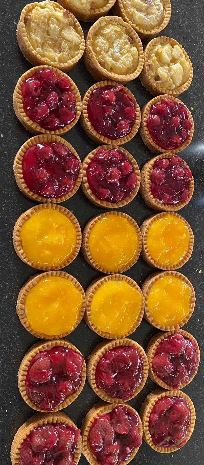Mini-fruittaartjes in papieren bekertjes. De vulling bestaat uit gele custard en rood fruit. 