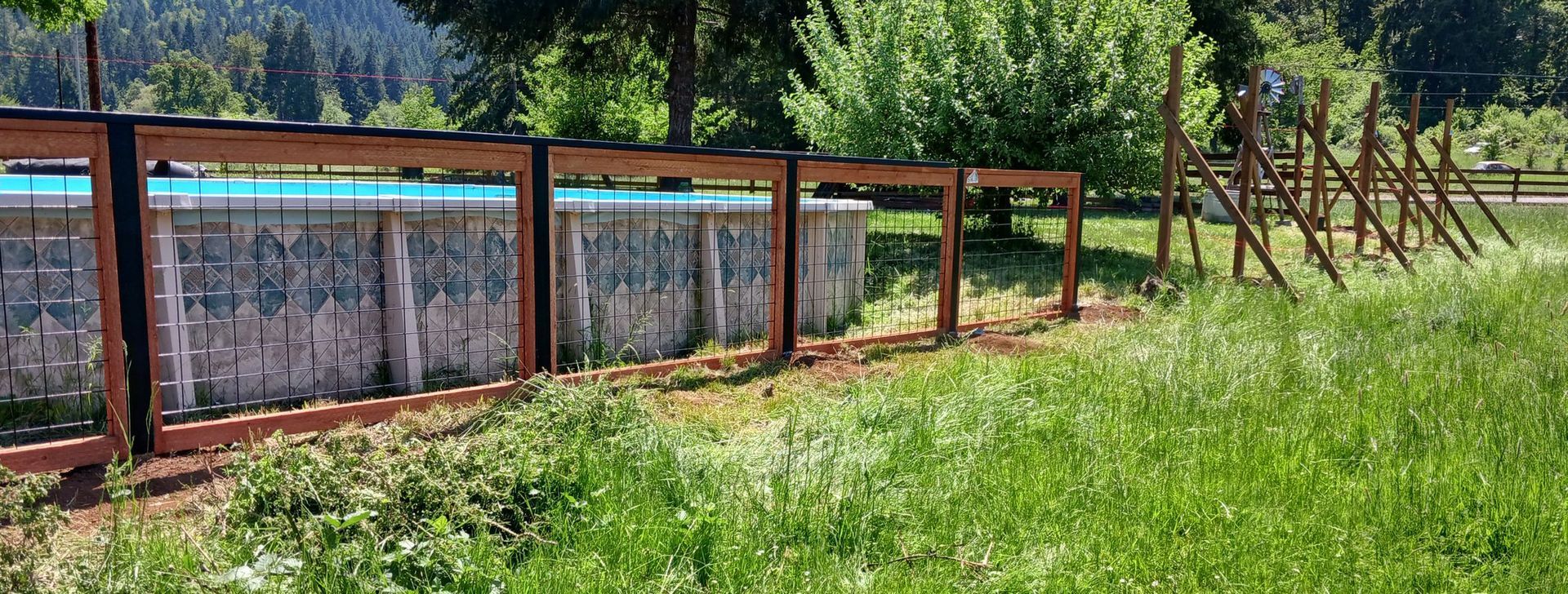 A wooden fence surrounds a swimming pool in a grassy field.