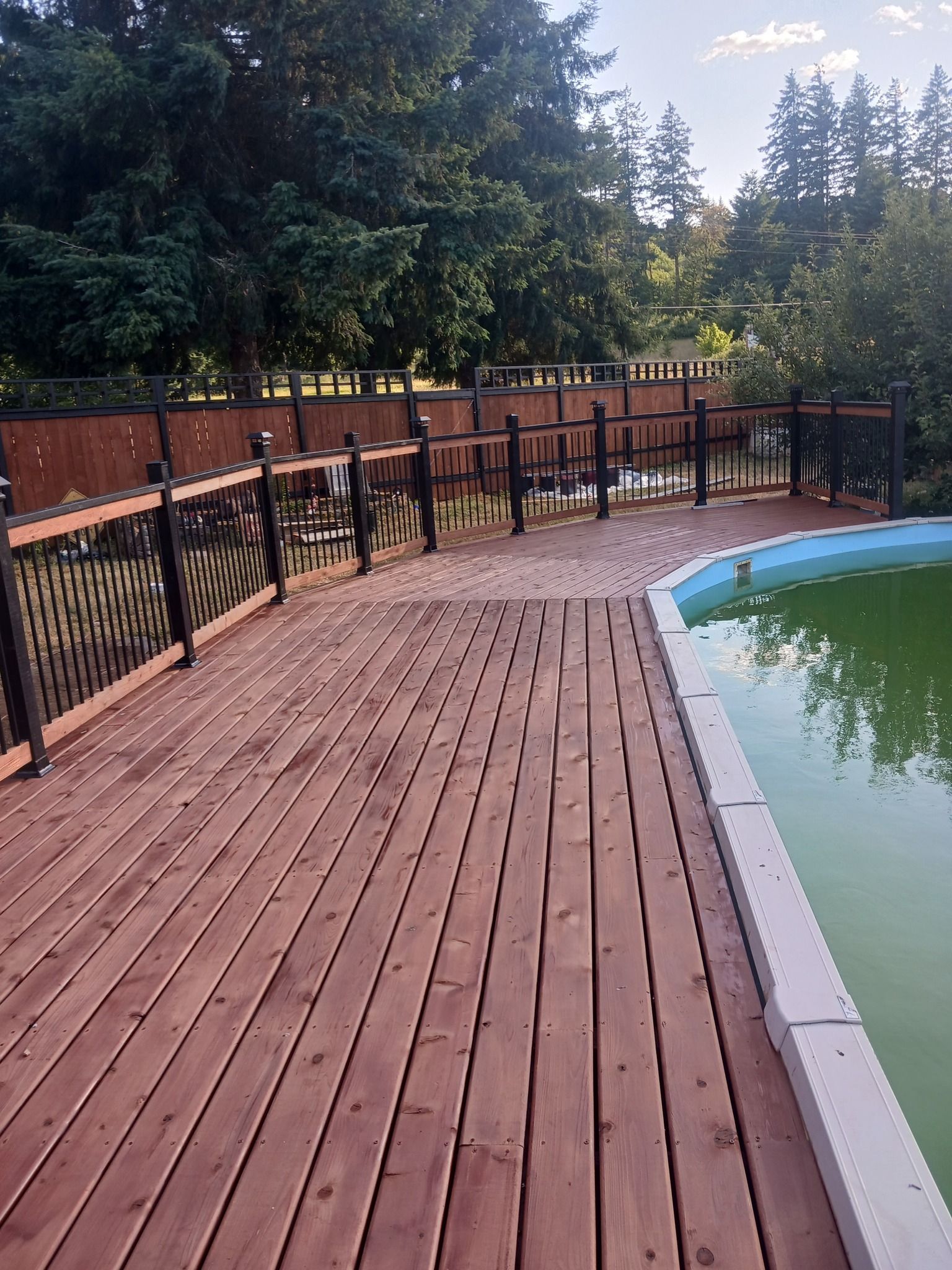A wooden deck next to a swimming pool with trees in the background