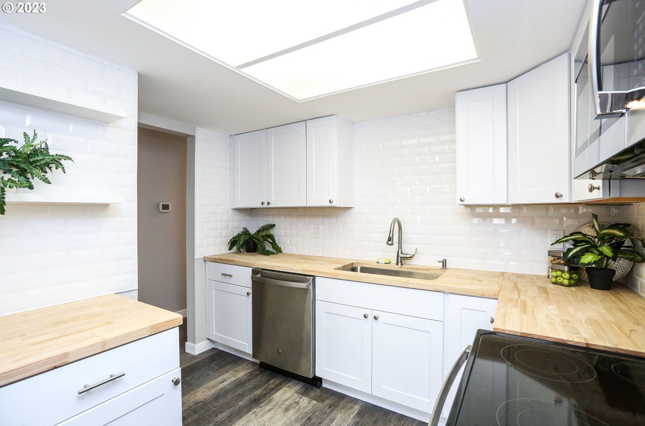 A kitchen with white cabinets , wooden counter tops , stainless steel appliances and a skylight.