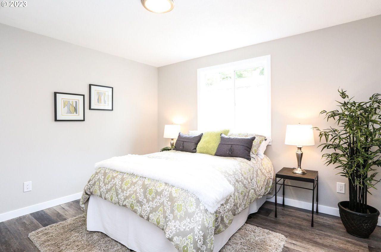 A bedroom with a bed , lamps , a plant and a window.