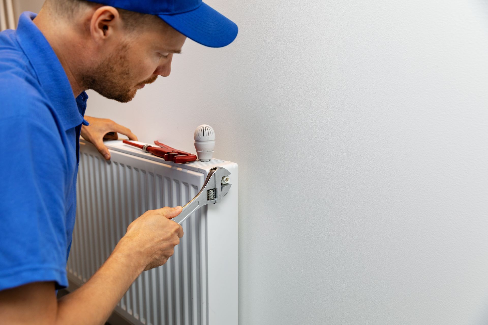 Un homme répare un radiateur avec une clé.
