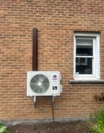 Un climatiseur blanc est monté sur le côté d'un bâtiment en briques à côté d'une fenêtre.