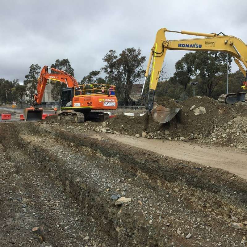 A Yellow Komatsu Excavator Is Working On A Dirt Road — Blackpoly Pipelines in Orange, NSW
