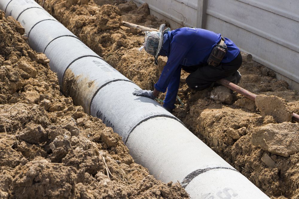 A Man Is Kneeling Down Next To A Pipe In The Dirt — Blackpoly Pipelines in Dubbo, NSW