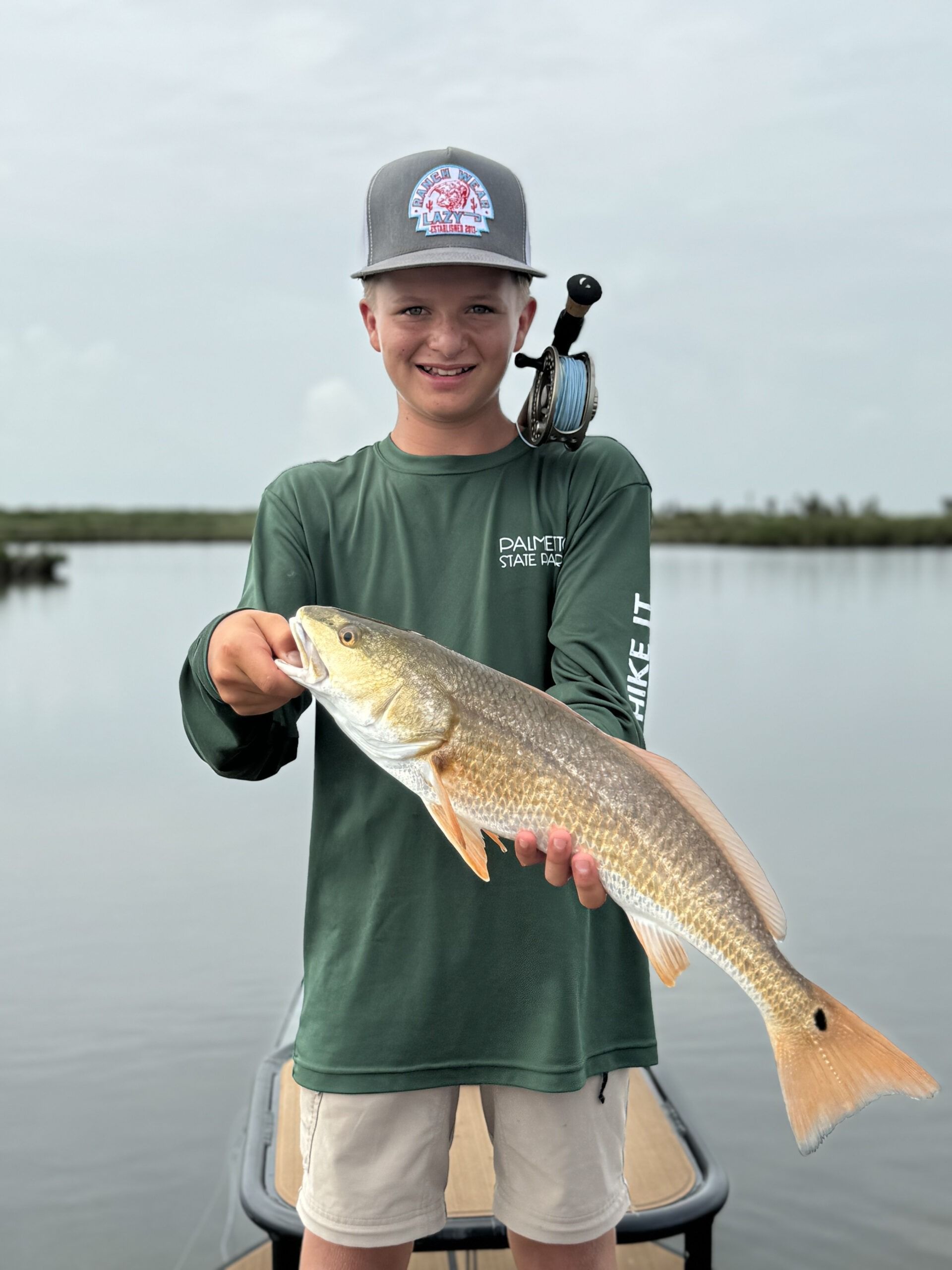 A young boy is standing on a boat holding a large fish.