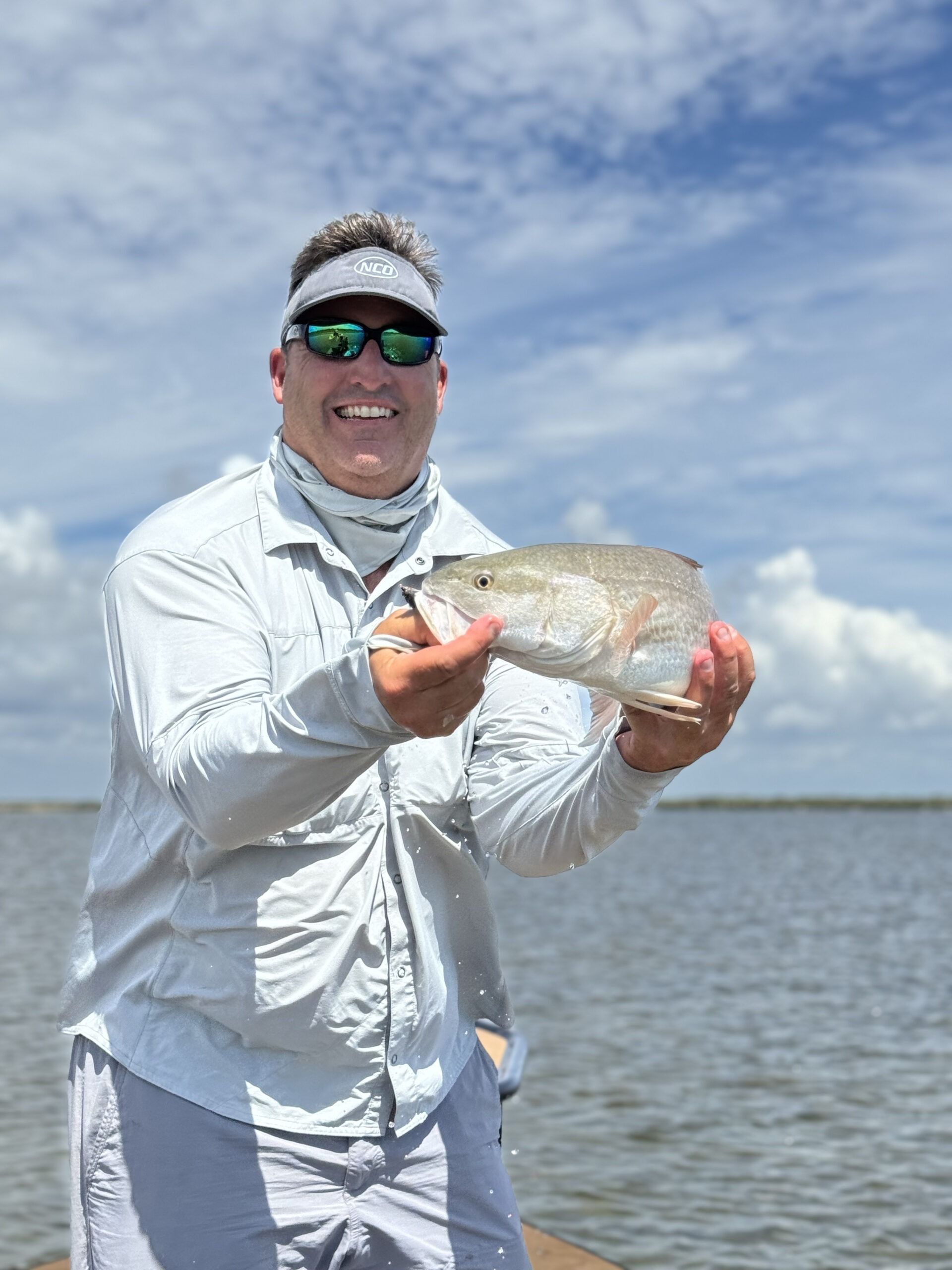 A man is holding a fish in his hands in front of a body of water.