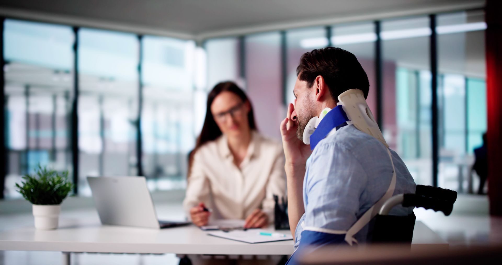 Two coworkers in an office meeting, one speaking while the other listens across a desk.
