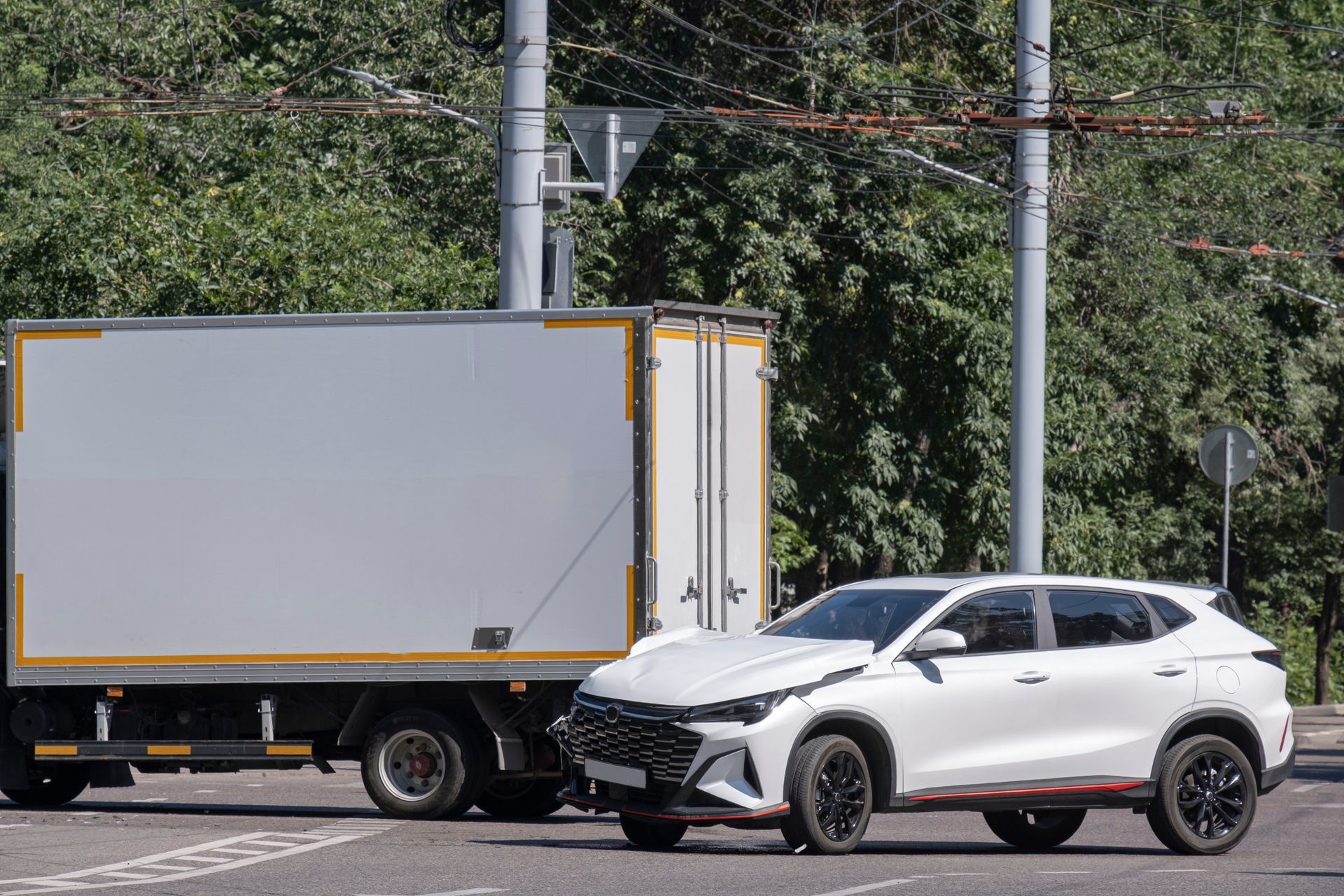 White SUV beside a gray box truck on a road, with trees and power lines in the background