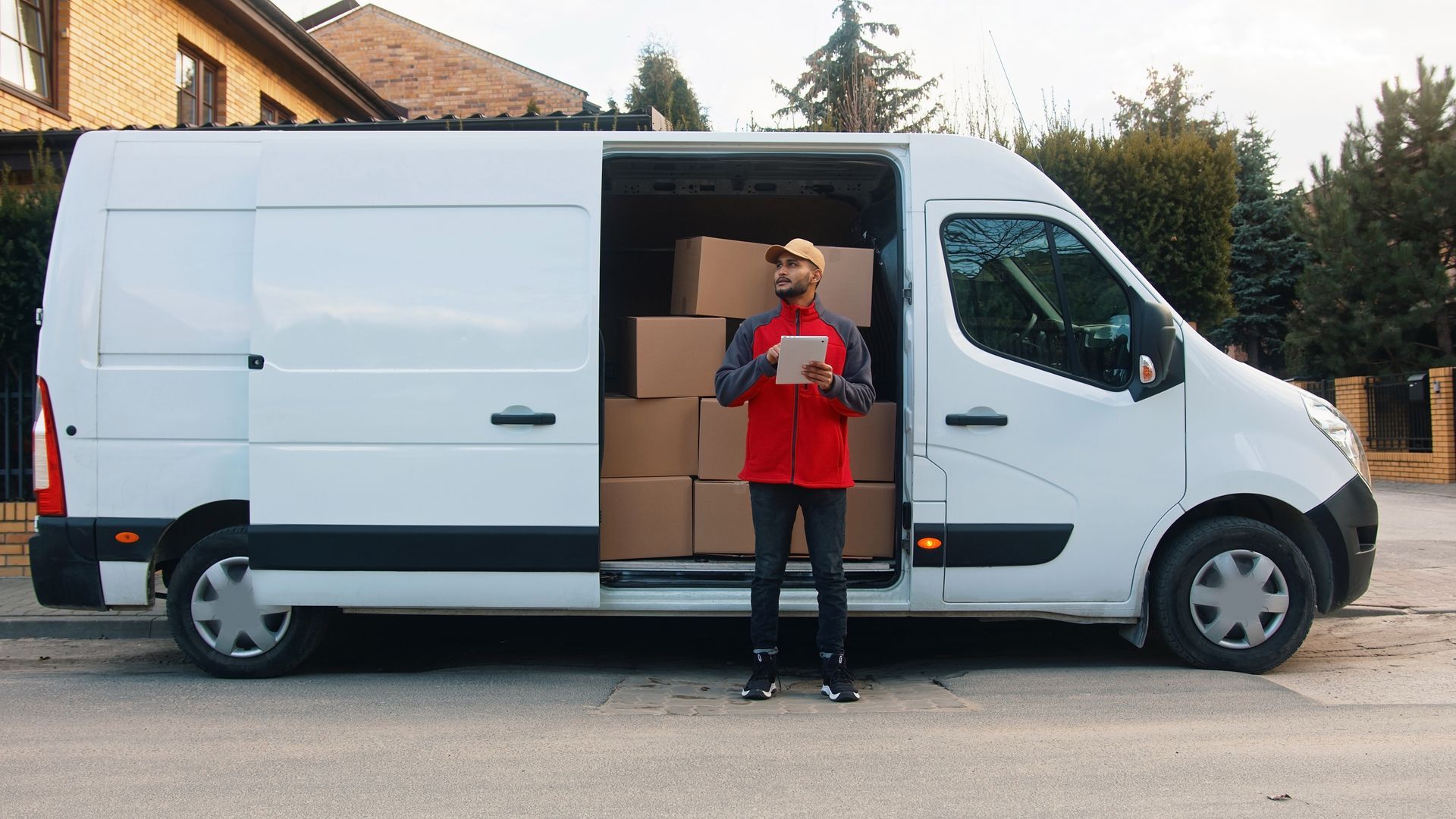 Delivery driver standing beside a white cargo van with its side door open and boxes inside.