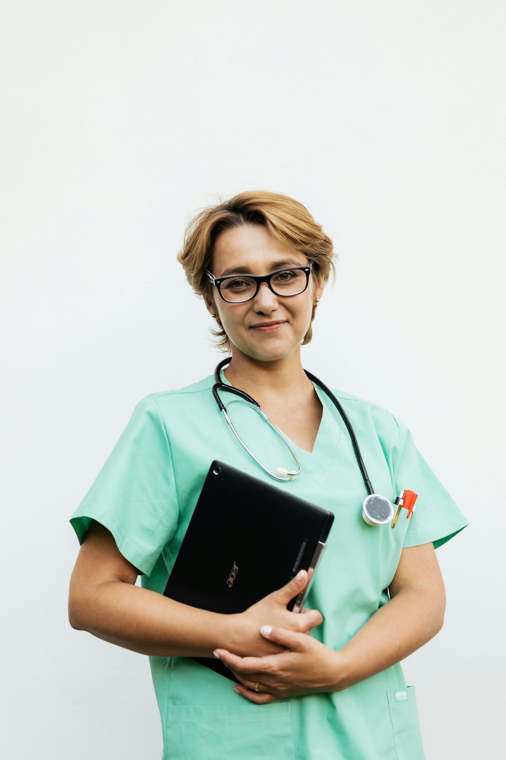 A Nurse in a green scrub is holding a laptop and a stethoscope.