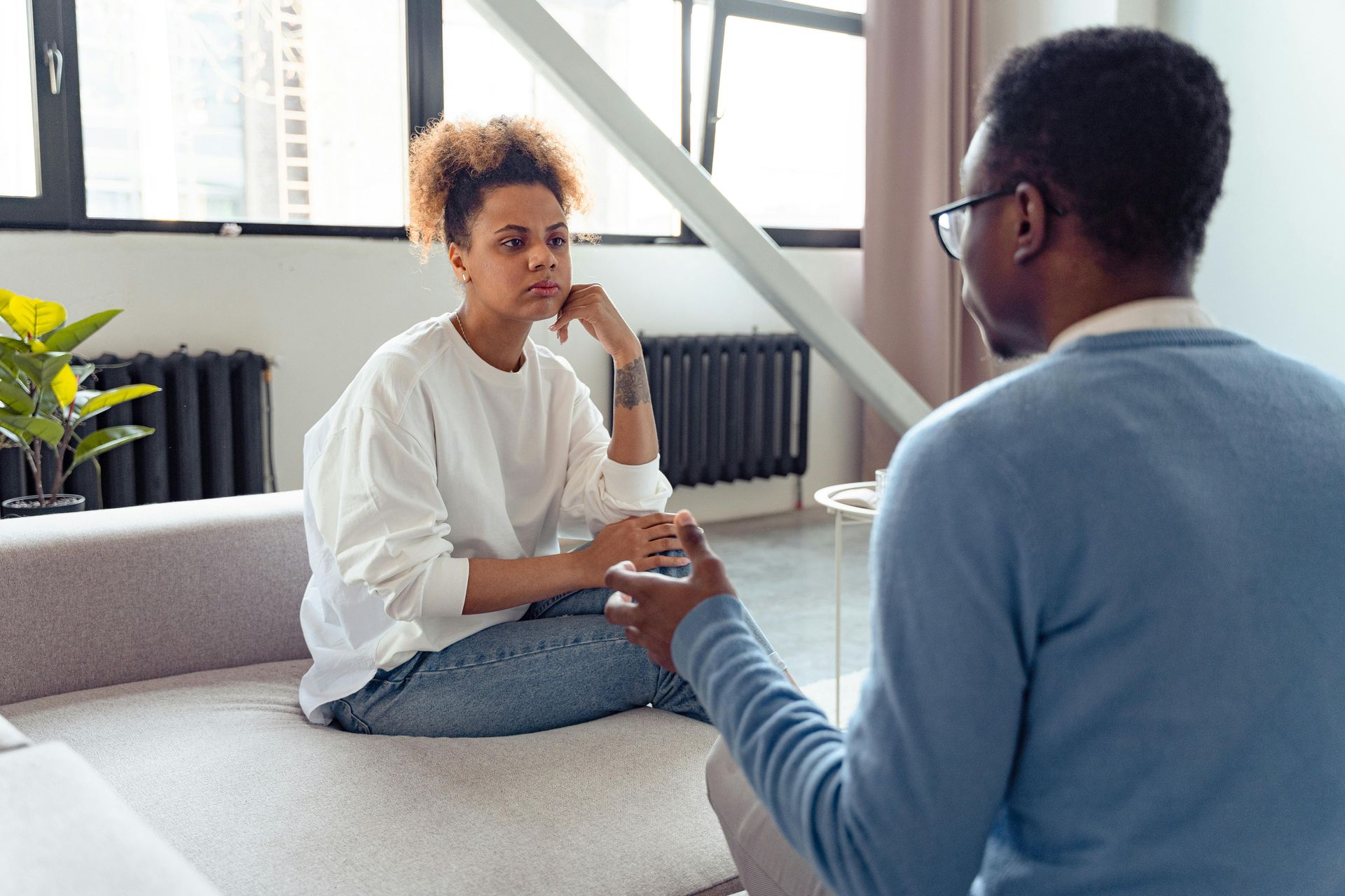 A man and a woman are sitting on a couch talking to each other.