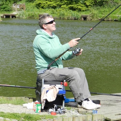 A man in a green sweatshirt is fishing in a lake