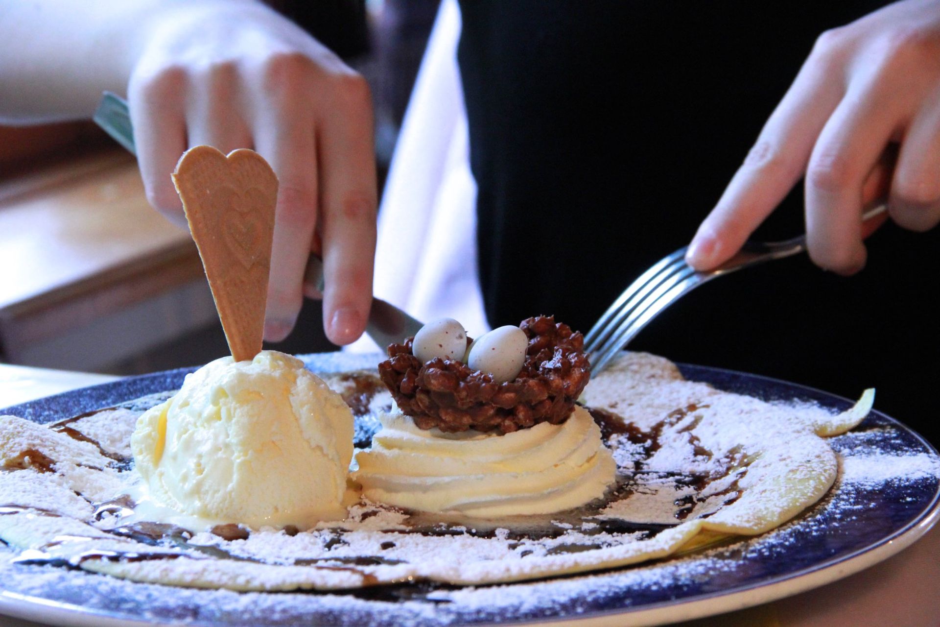 A person is cutting a dessert with ice cream and powdered sugar