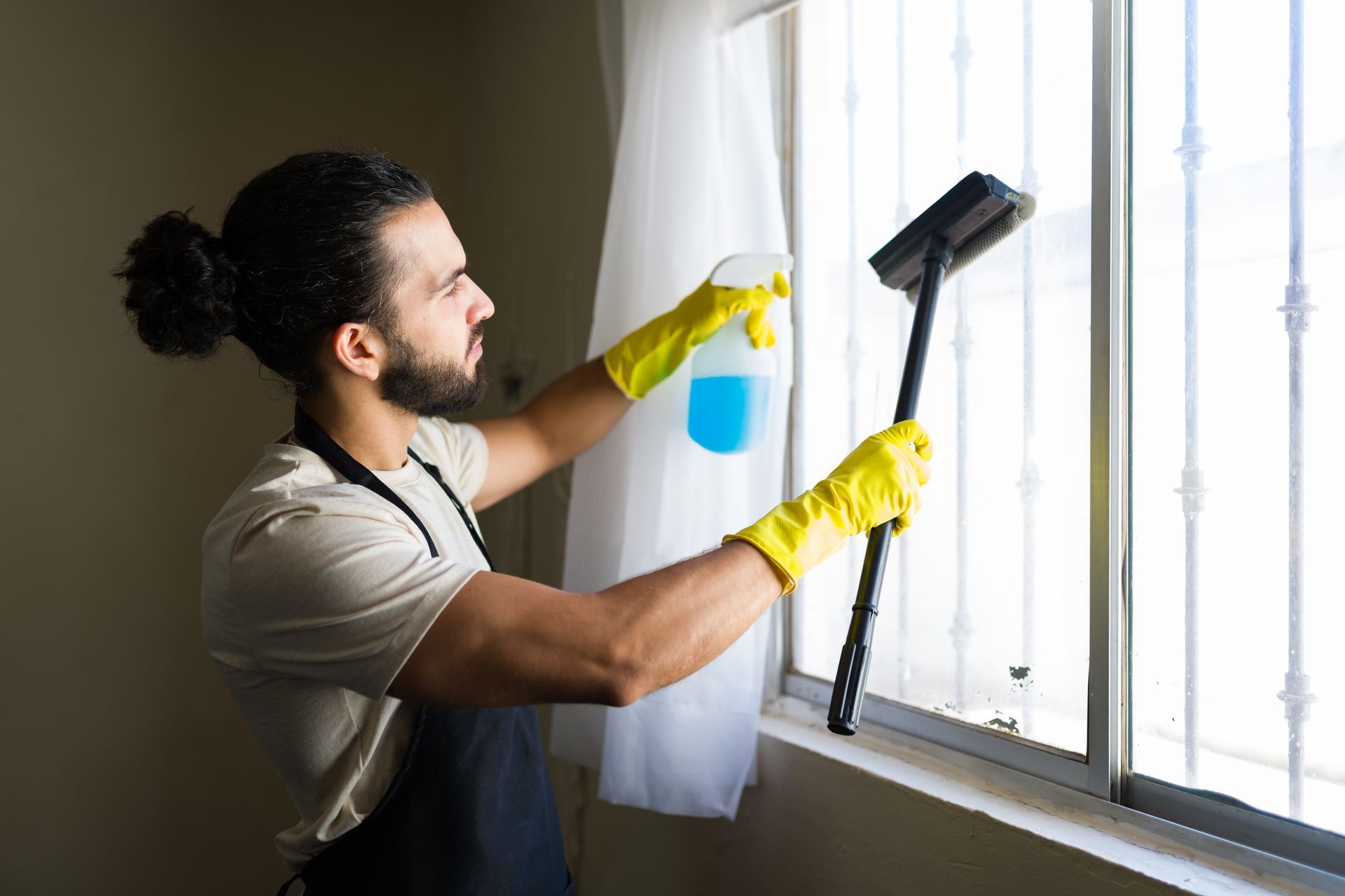 Young male window cleaner at a residential site, wearing apron and yellow gloves. Young male window cleaner at a residential site, wearing apron and yellow gloves.