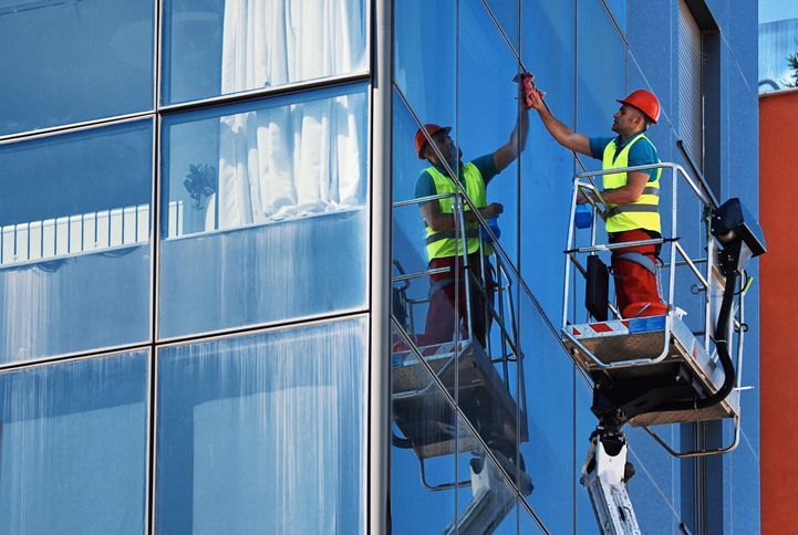 A window washers cleaning the outside of a commercial building during the day. A window washers cleaning the outside of a commercial building during the day.