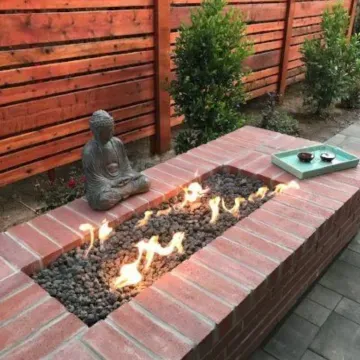 Brick outdoor fire pit with lava rocks, Buddha statue, and a tray with cups | Landscaper in Davis, CA
