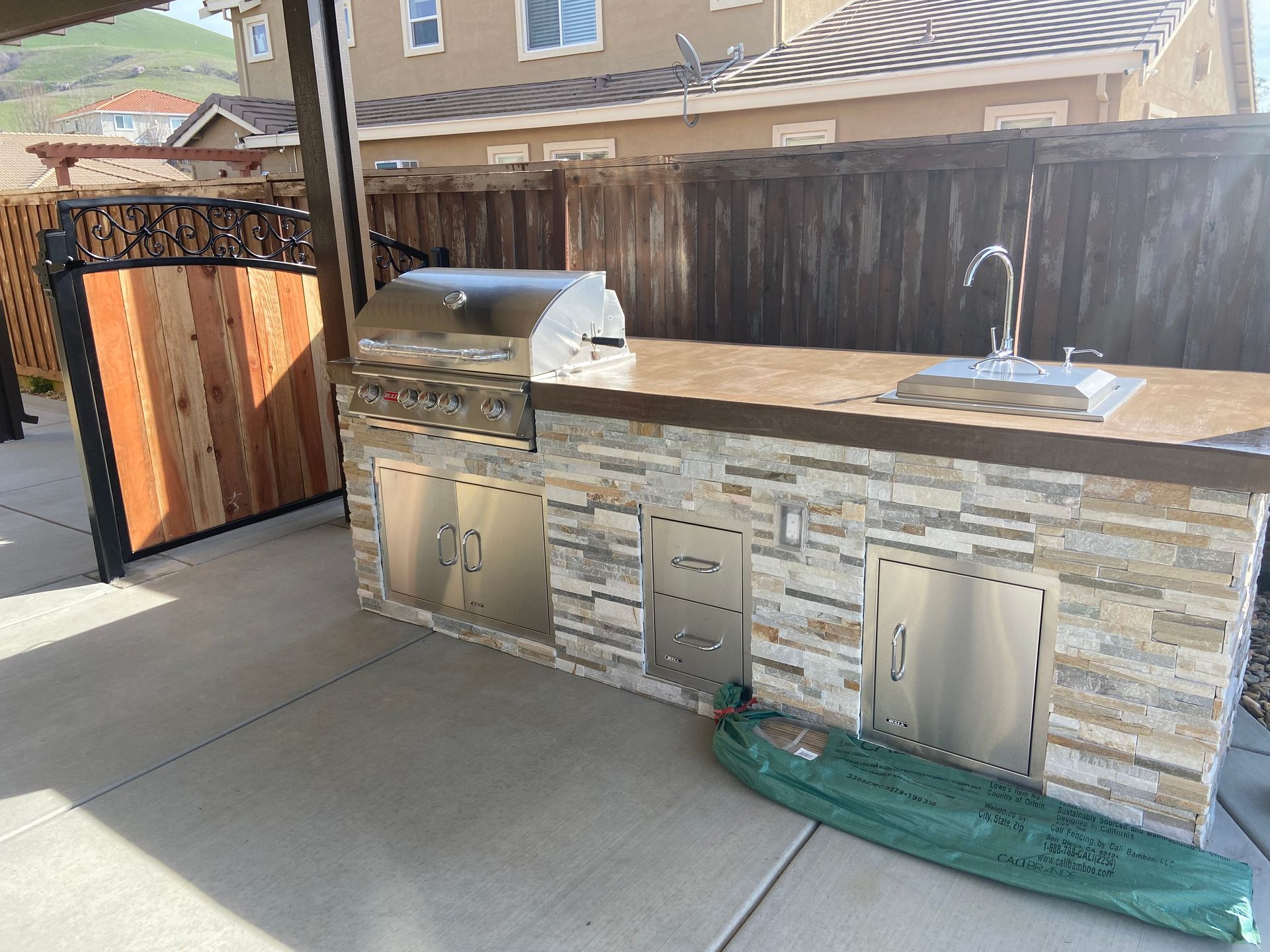 Modern outdoor kitchen design with a built-in stainless steel grill, stone countertop, and sink for outdoor cooking.
