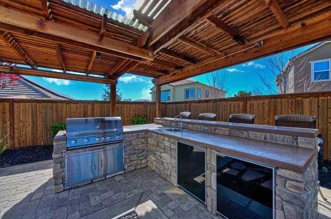 A large outdoor kitchen with a grill and a wooden pergola by Turfworks Inc., the top landscaping company in Vacaville, CA