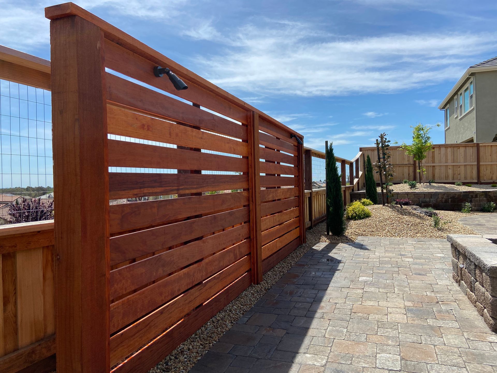 A wooden fence is surrounding a brick patio in a backyard.