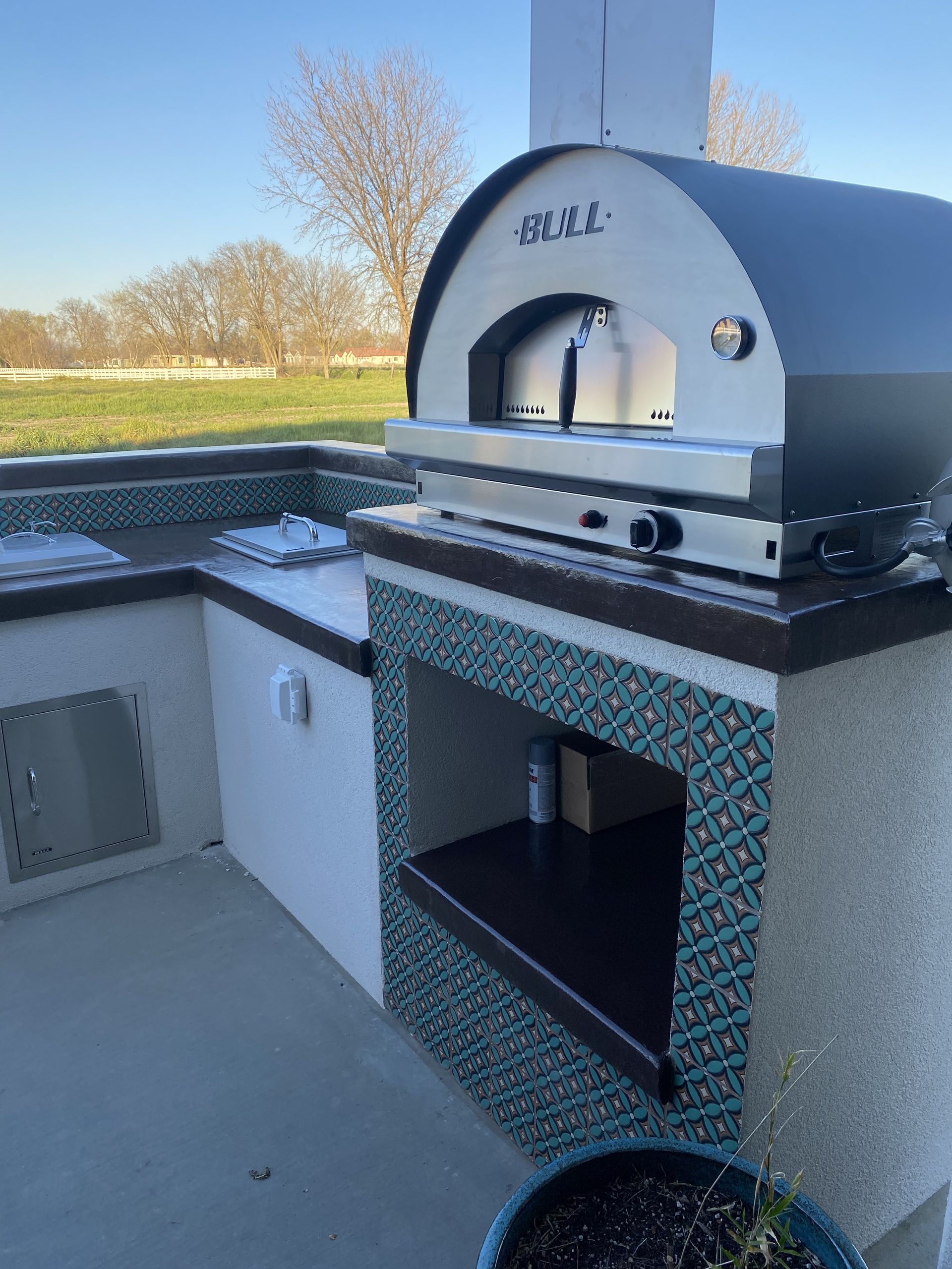 An outdoor kitchen with a pizza oven and a potted plant