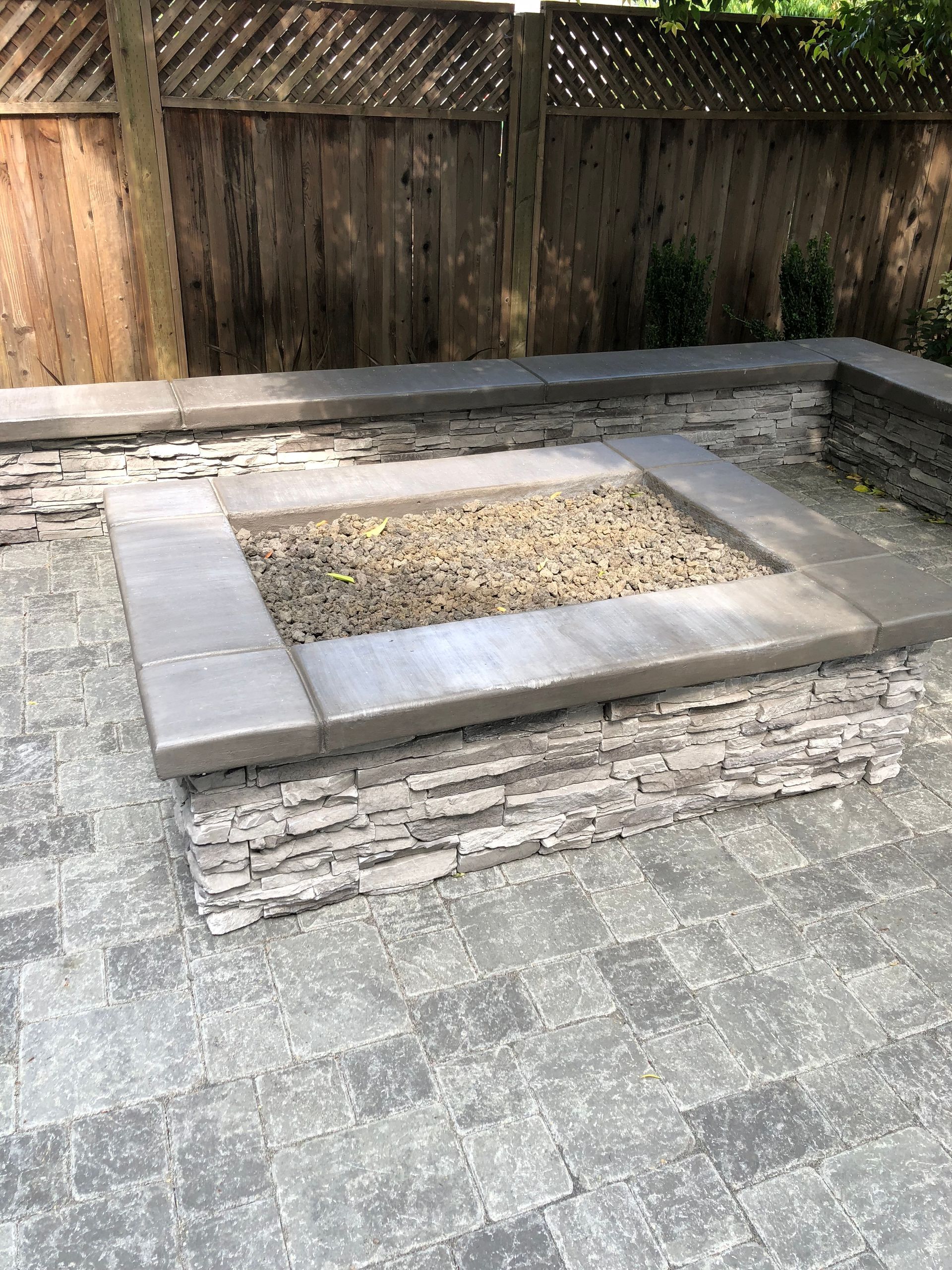 A landscape design in Davis, CA, with a fire pit, that sits on a patio next to a wooden fence.