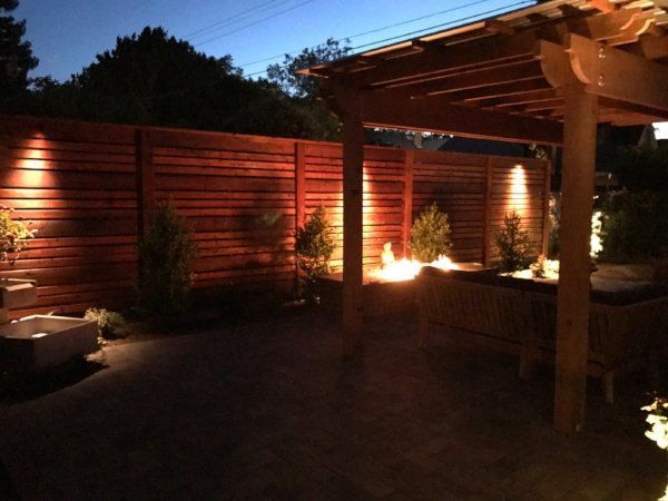A backyard landscaped by Turfworks, Inc. with a pergola adorned in elegant lighting, casting a warm ambiance at night