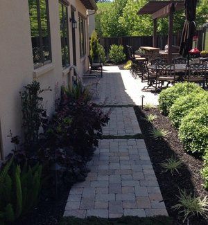 Charming backyard landscape design with a stone walkway, lush greenery, and an outdoor dining area with a pergola.