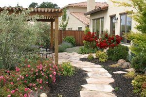 A stone walkway leading to a house with a pergola and flowers | Landscape Design in Davis, CA