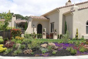 Lovely front yard landscape design in Vacaville, CA, with colorful plants, subtle rocks, and a Mediterranean-style home.