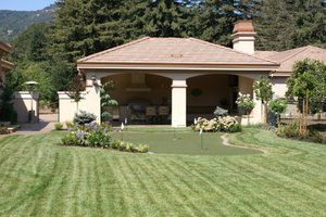 Stunning backyard landscape design with a lush green lawn, colorful garden beds, and a covered outdoor living area.